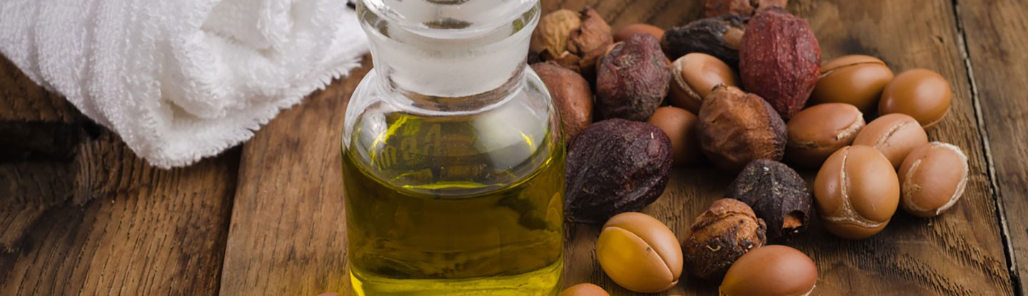 A picture of a bottle of macademia oil on a table with a selection of nuts surrounding it