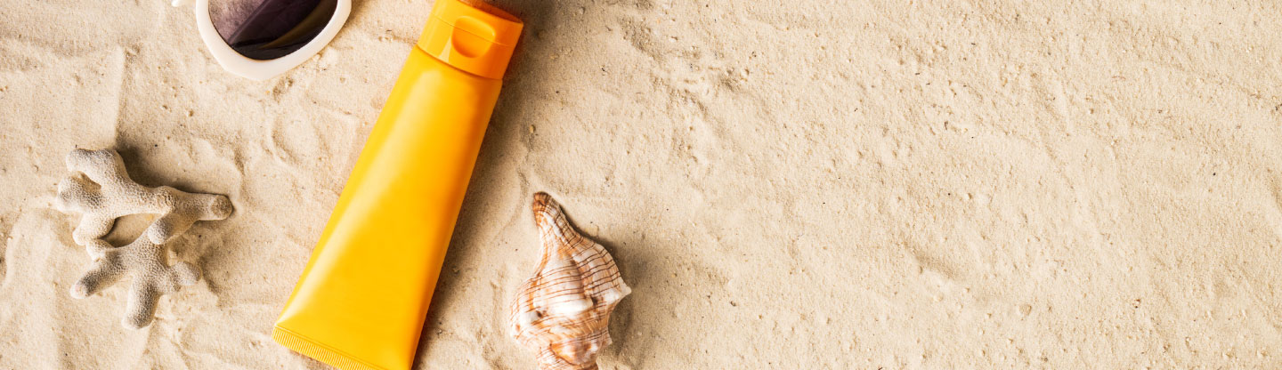 A tube of suncream in the sand with seashells