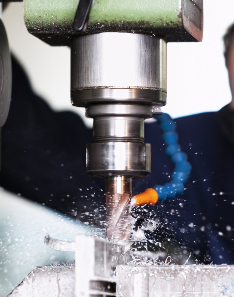 Metalworking fluid spraying on the bit of a drill press that is drilling through metal