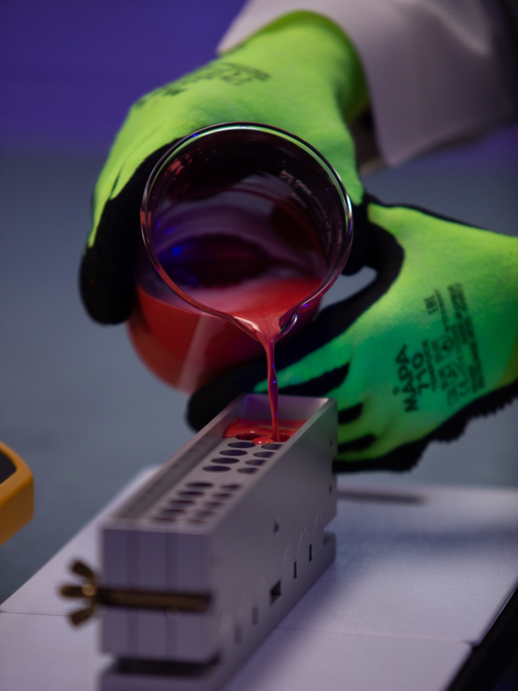 Gloved hands pouring a red formulation into a mold.